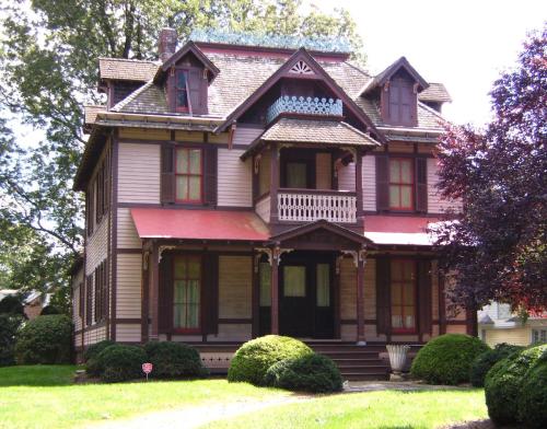 A large, Victorian-style house with a pink exterior, intricate woodwork, and a lush green lawn.