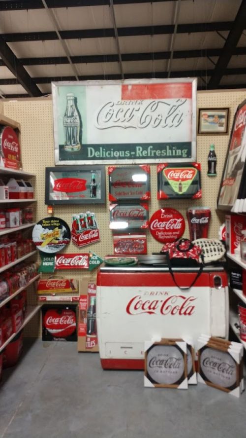 Vintage Coca-Cola memorabilia displayed on a wall, featuring signs, bottles, and a retro cooler.