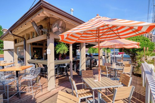 A sunny outdoor dining area with striped umbrellas, tables, and a lively atmosphere at a restaurant.