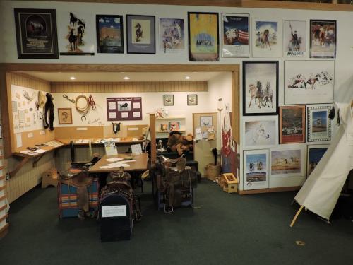 A cozy exhibit space featuring western-themed artwork, a display table, and saddle-related items on the walls.