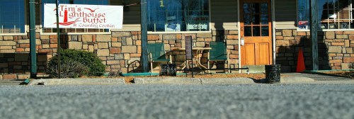 Exterior view of Tim's Lighthouse Buffet, featuring a stone facade and a sign, with empty tables outside.
