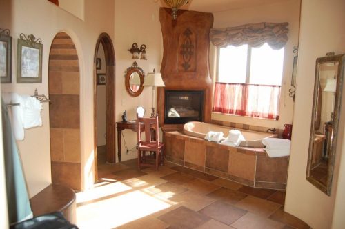 Spacious bathroom with a large tub, fireplace, and natural light, featuring warm tones and elegant decor.