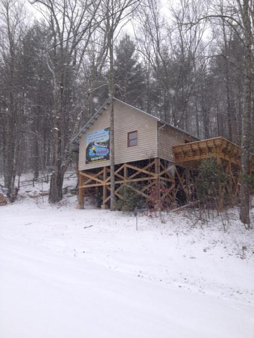 A wooden house on stilts surrounded by snow-covered trees, with a colorful banner on the side.