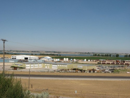 A rural industrial area with several buildings, storage units, and fields under a clear blue sky.