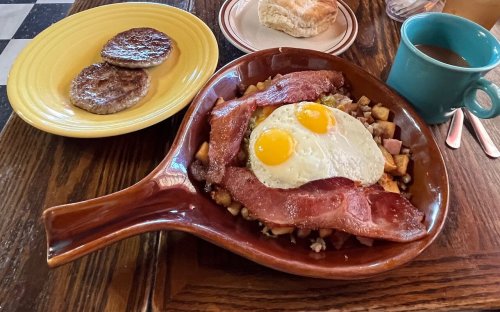 A hearty breakfast plate with bacon, eggs, potatoes, and sausage, alongside a cup of coffee and a biscuit.