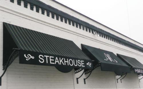 Black and white striped awnings over a restaurant facade, featuring "STEAKHOUSE" and "BAR" signage.