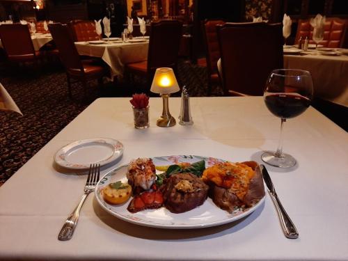 A beautifully plated meal featuring seafood, stuffed potato, vegetables, and a glass of red wine on a white tablecloth.