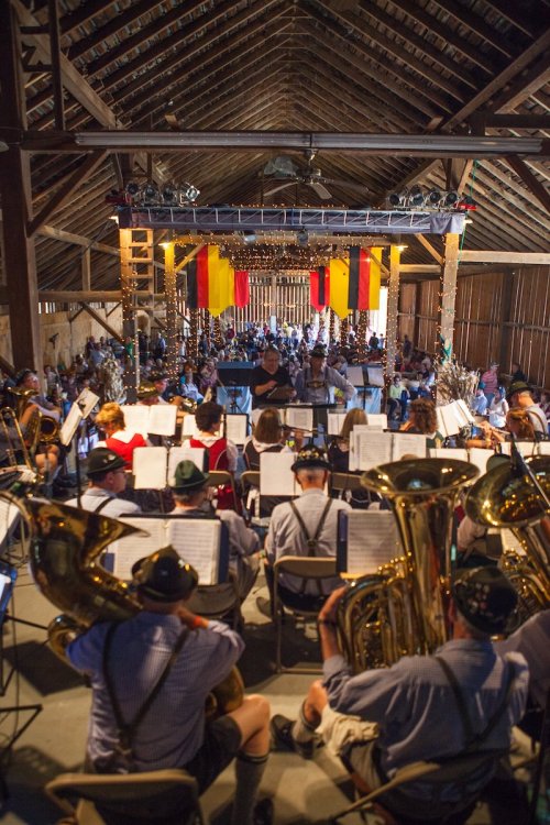 A lively barn scene with musicians playing instruments, colorful banners hanging, and a crowd enjoying the performance.