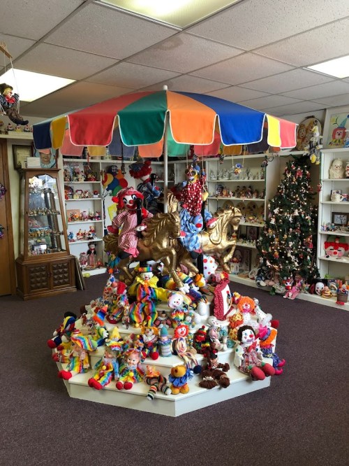 A colorful carousel with golden horses surrounded by various clown dolls and a decorated Christmas tree in the background.