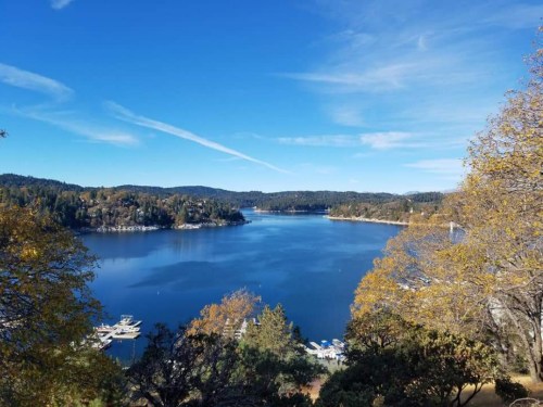 Scenic view of a calm lake surrounded by trees and hills under a clear blue sky.