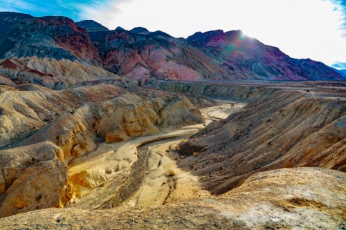 A colorful, rugged landscape of mountains and valleys under a bright sky, showcasing the natural beauty of a desert region.