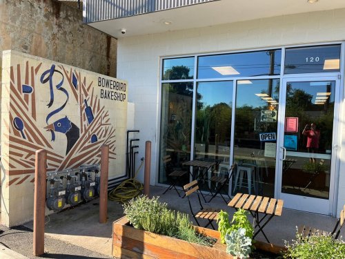 Exterior of Bowerbird Bakeshop featuring a mural, open sign, and outdoor seating area.