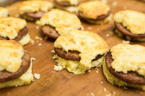 Freshly baked biscuits filled with sausage patties, arranged on a wooden surface.