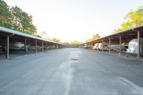 A wide view of a boat storage facility with covered spaces and parked boats on either side, illuminated by soft sunlight.