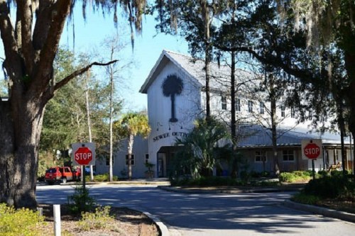 A building with a sign reading "Sewer Outlet" surrounded by trees and stop signs on a sunny day.