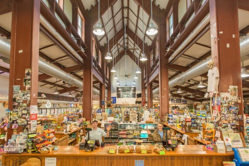 A spacious market interior with high ceilings, wooden counters, and two staff members at the checkout.