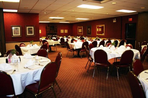 A dining room with round tables set with white tablecloths and red chairs, ready for an event or gathering.