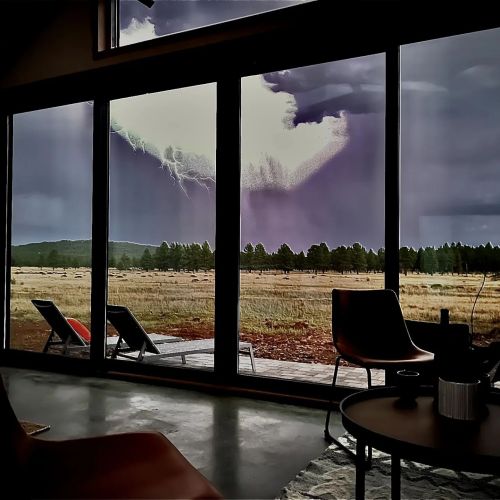 A dramatic view of lightning striking outside through large windows, with a cozy interior and outdoor seating visible.