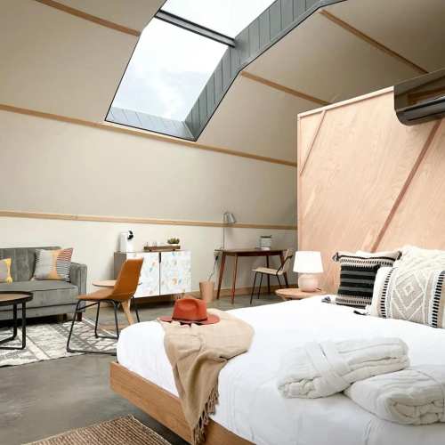 Cozy interior with a skylight, wooden accents, a seating area, and a bed adorned with blankets and pillows.