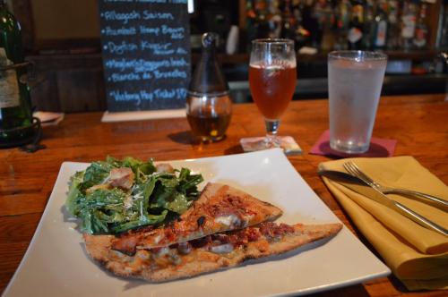 A plate with two pieces of fish, a side salad, and a drink on a bar counter.