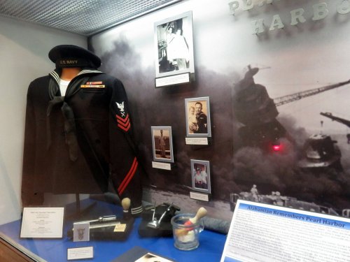 Display case featuring a U.S. Navy uniform, photographs, and artifacts related to Pearl Harbor.
