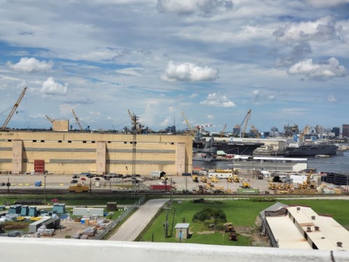 A busy industrial port with cranes, ships, and warehouses under a partly cloudy sky.