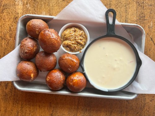 A tray with golden-brown fried balls, a small bowl of mustard, and a cast-iron dish of creamy sauce on parchment paper.