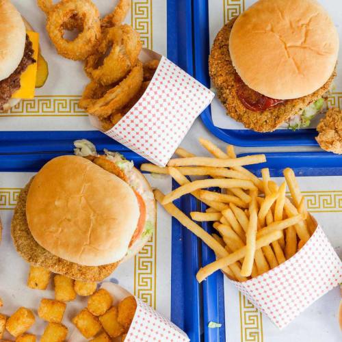 A colorful spread of burgers, onion rings, and fries on blue trays with a patterned border.