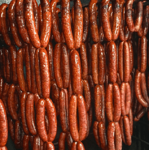 A close-up of hanging sausages, showcasing their rich, reddish-brown color and glossy texture.