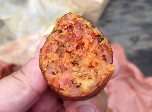Close-up of a hand holding a partially bitten sausage, revealing a textured, meaty interior.