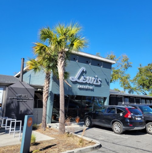 Exterior of Lewis Barbecue with palm trees and clear blue sky, featuring a parking area and outdoor seating.