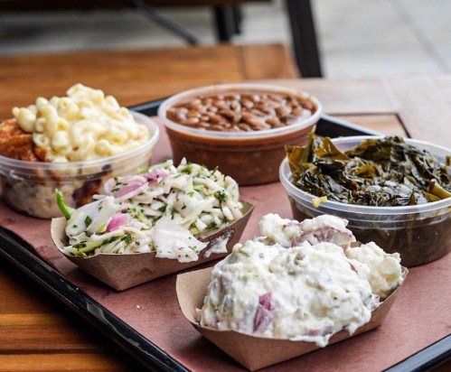 A tray with four containers of side dishes: macaroni, baked beans, collard greens, and two types of coleslaw.