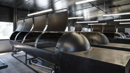 Industrial kitchen with large black smokers lined up against the wall, featuring domed lids and metal grates.