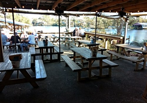 Outdoor dining area with wooden picnic tables, string lights, and a view of a waterway in the background.