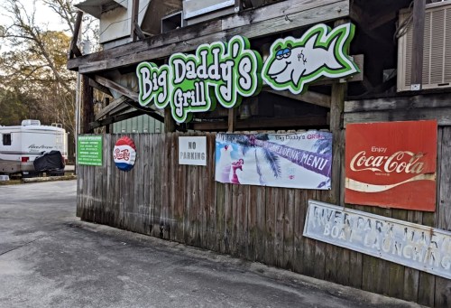 Sign for "Big Daddy's Grill" on a wooden building, with nearby signs for parking and boat launching.