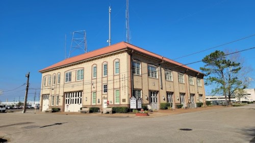 Historic brick building with a red roof, antennas, and large windows, set against a clear blue sky.