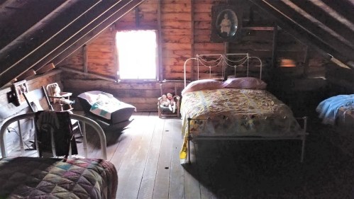 Cozy attic bedroom with two beds, a rocking chair, and vintage decor, featuring wooden beams and a warm atmosphere.
