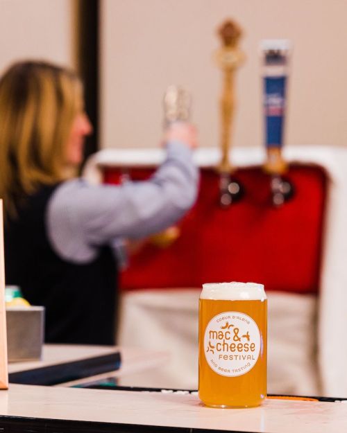 A glass of beer in front of a festival booth, with a person pouring from a tap in the background.