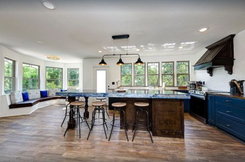 Modern kitchen with a large island, bar stools, and ample windows, featuring a cozy seating area and stylish decor.