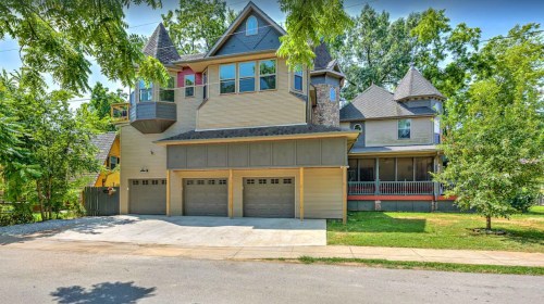 A large, multi-story house with a unique design, featuring a garage and surrounded by trees and greenery.