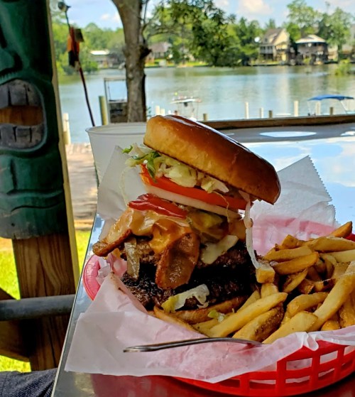 A juicy burger with toppings and fries, set against a scenic lakeside view.