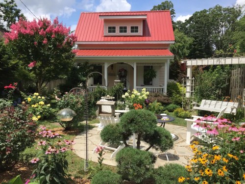 A charming house with a red roof surrounded by a vibrant garden filled with flowers and greenery.