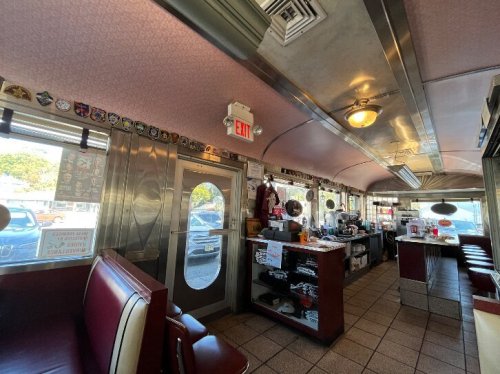 Interior of a retro diner featuring red booths, a counter, and vintage decor, with large windows and a welcoming atmosphere.