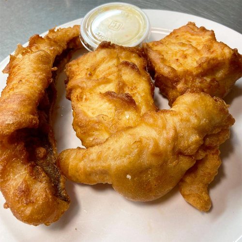 Three pieces of golden-brown fried fish on a plate, accompanied by a small container of dipping sauce.