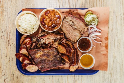 A platter of assorted barbecue meats, including brisket, sausage, and ribs, served with sides of beans, rice, and pickles.