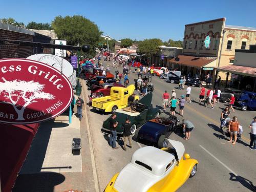 A bustling street filled with classic cars and people enjoying a car show on a sunny day.