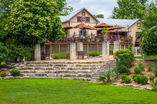 A charming restaurant with outdoor seating, surrounded by greenery and stone steps leading to a grassy area.