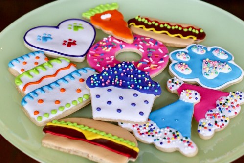 A colorful assortment of decorated cookies shaped like hearts, donuts, cupcakes, and hot dogs on a green plate.