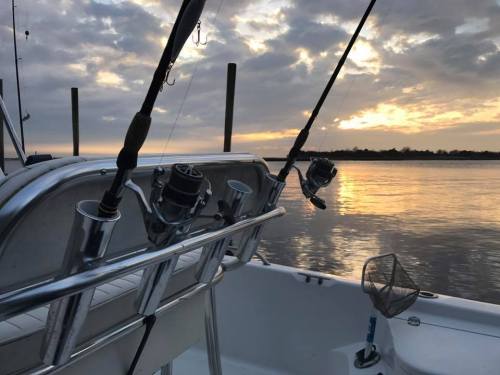 Fishing rods are mounted on a boat, with a serene sunset reflecting on the water in the background.