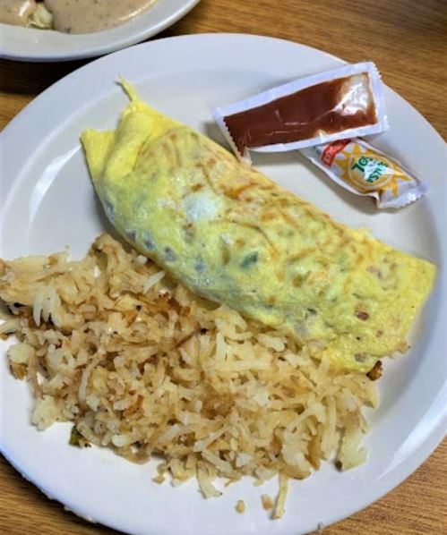 A plate with a folded omelet, hash browns, and two condiment packets.